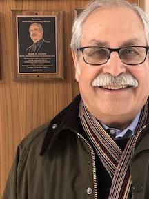 man poses for photo in front of alumni award