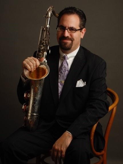 A man sits in a chair and props a saxophone on one knee.