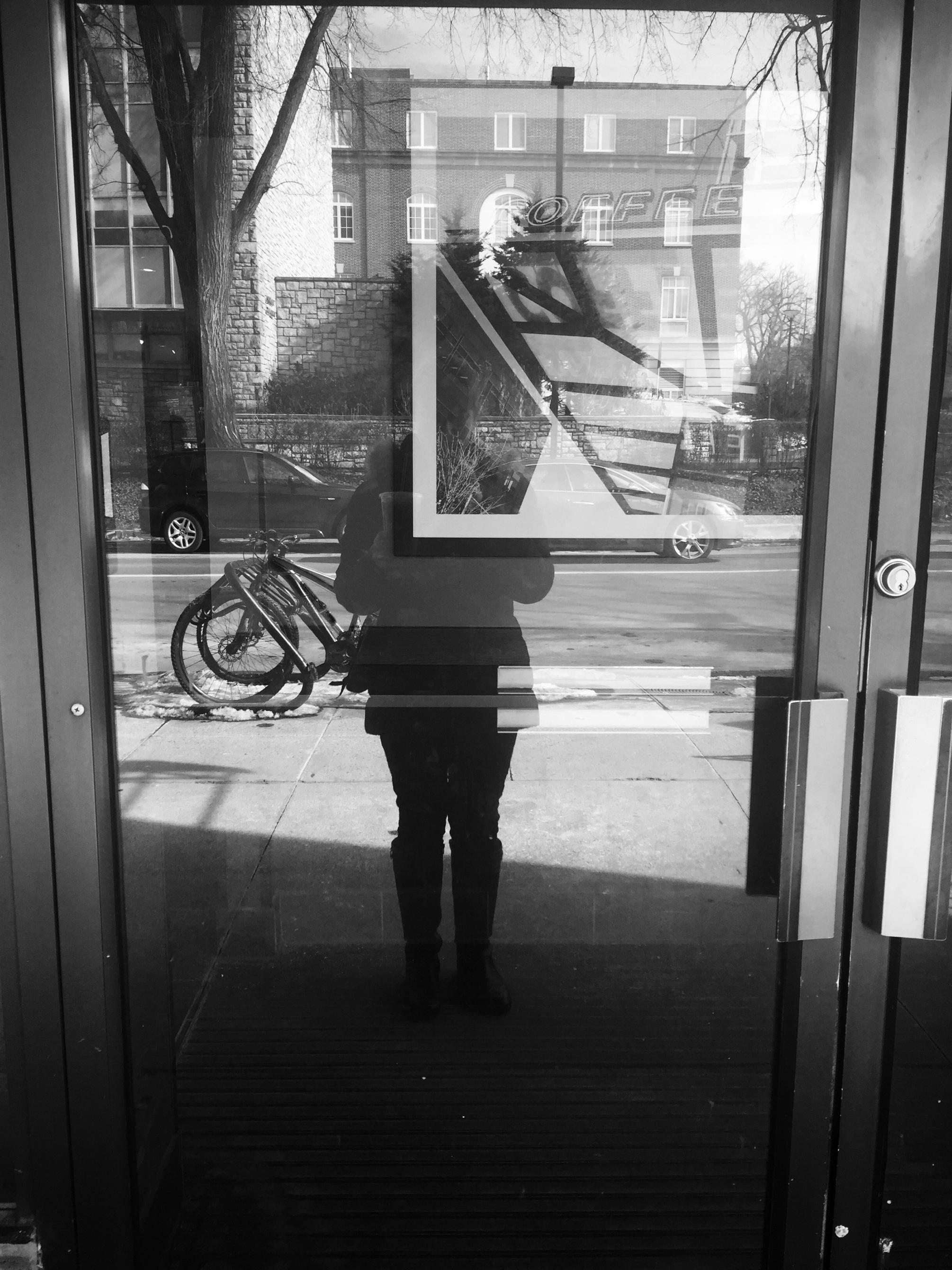 Selfie photograph of Emily Strohm's reflection in a glass door. 