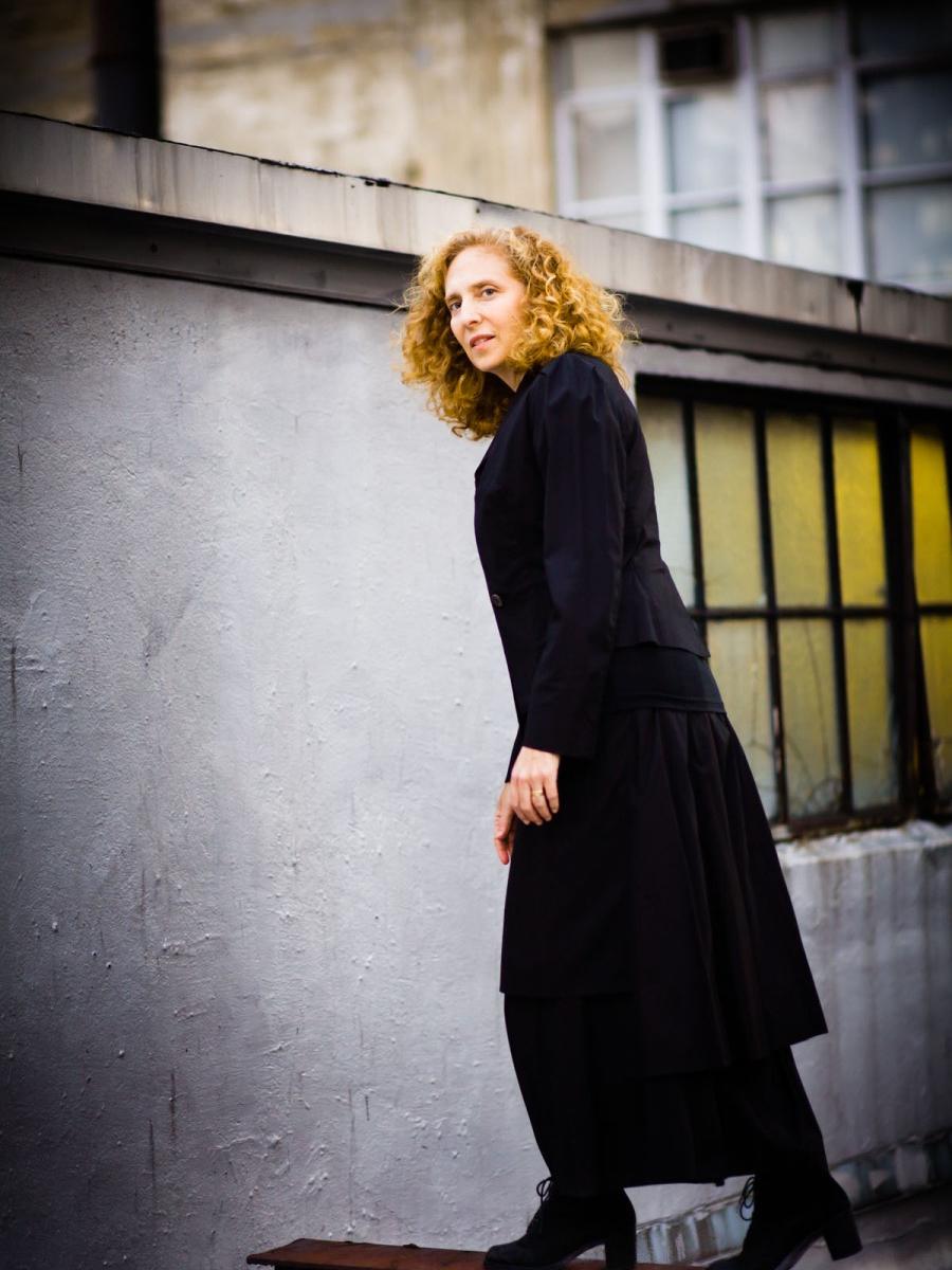 Composer Julia Wolfe stands on a ledge and lunges forward while she looks at the camera.