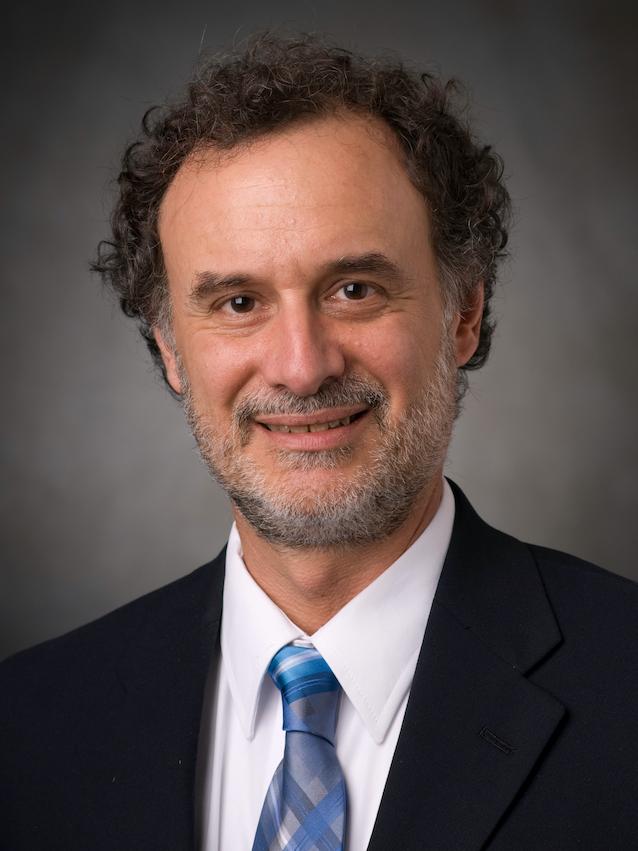 A man wearing a suit and tie smiles for a professional headshot.
