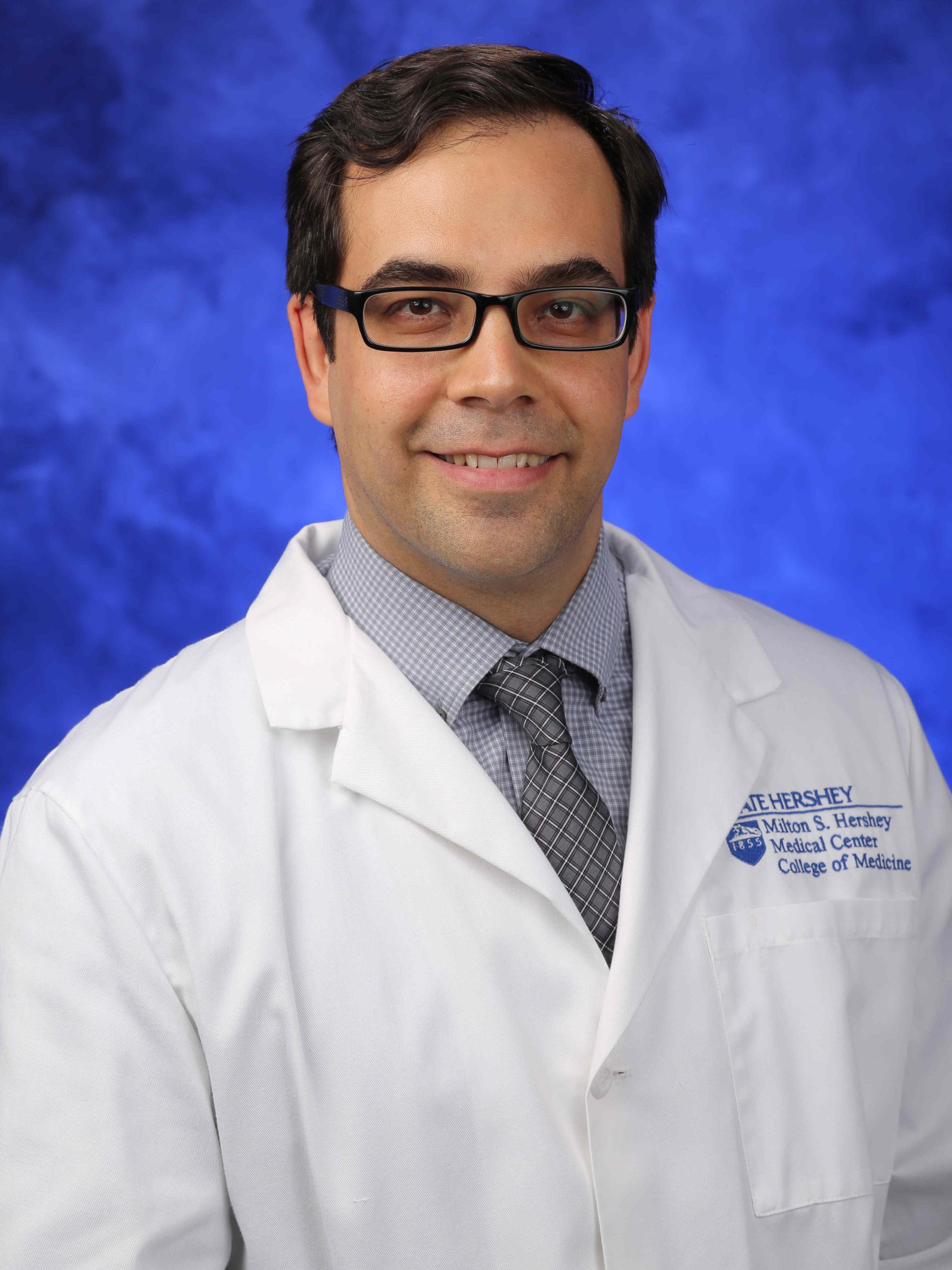 Dr. Alfredo Bellon poses for a professional photo, wearing a tie and a physician's coat.