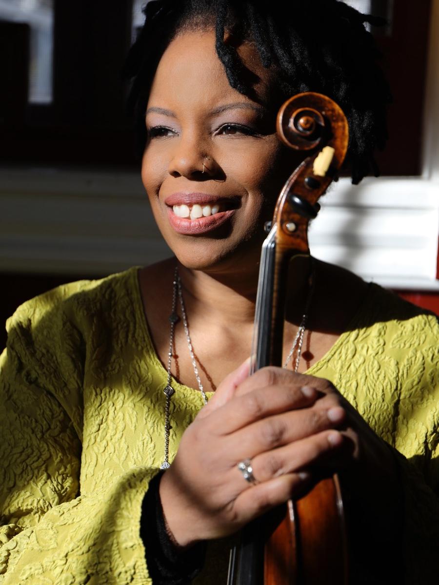 A woman holds her violin at the neck while she smiles and looks off to her right.