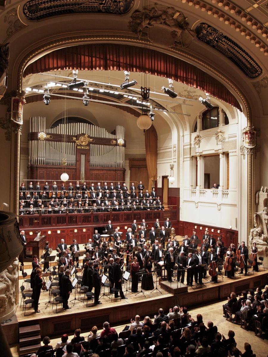 Members of a symphony orchestra stand on the stage of a grand music hall.