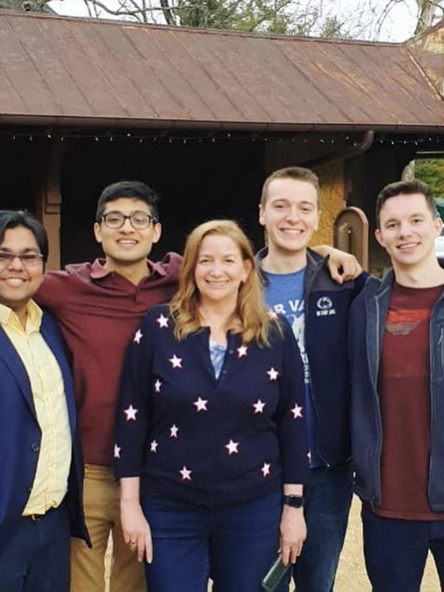 A young group of men stands smiling with the program director, a red-haired woman.