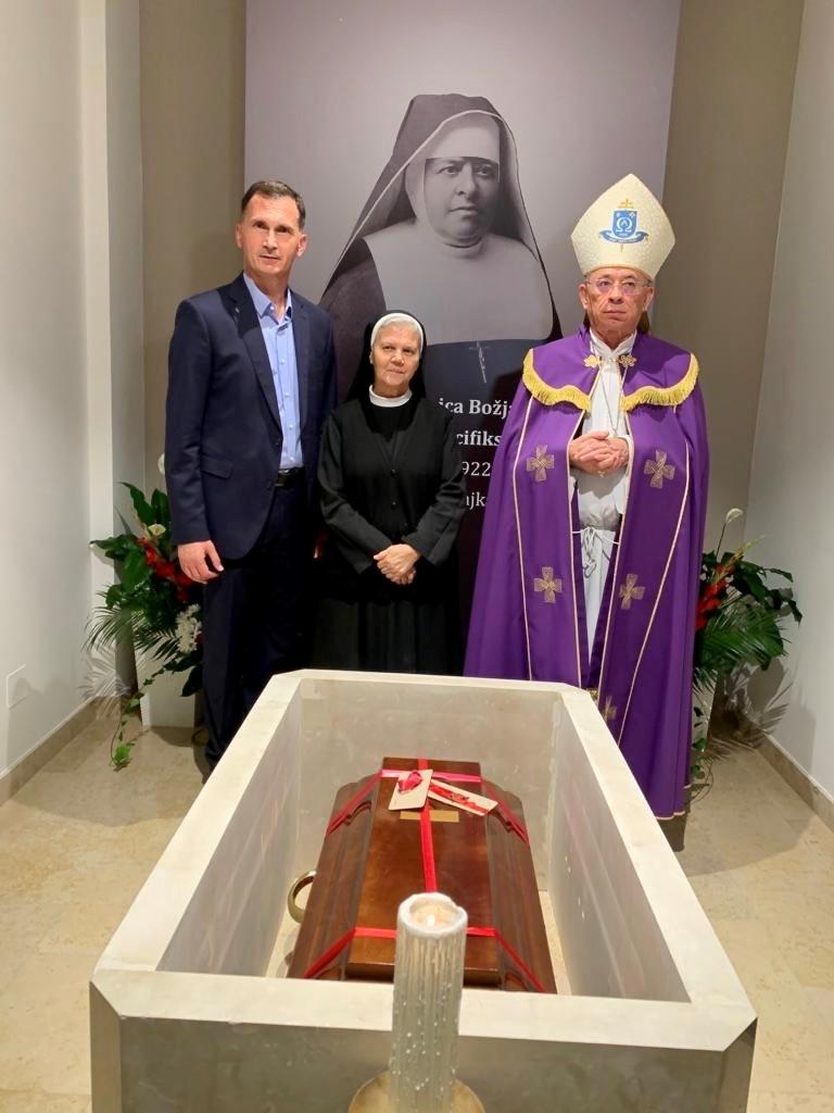 Three people - a man, a nun, and a bishop - stand over a coffin