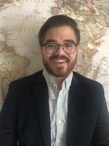 student standing in front of a world map in formal entire, smiling and posing for photo