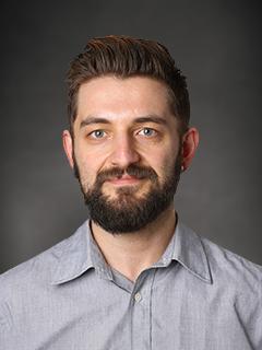 professor in collared shirt smiles and poses for professional headshot