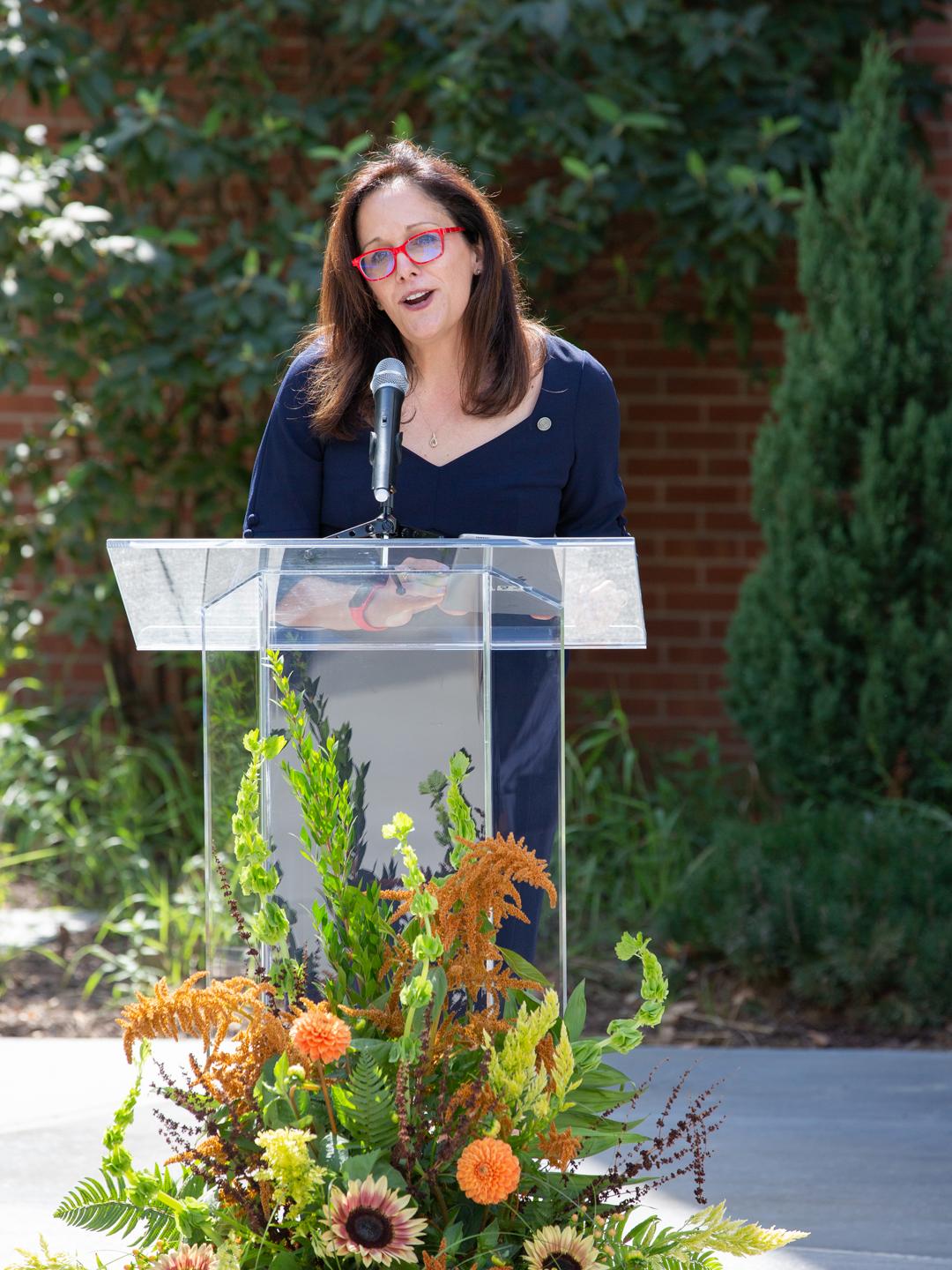 woman standing behind clear podium talking into microphone