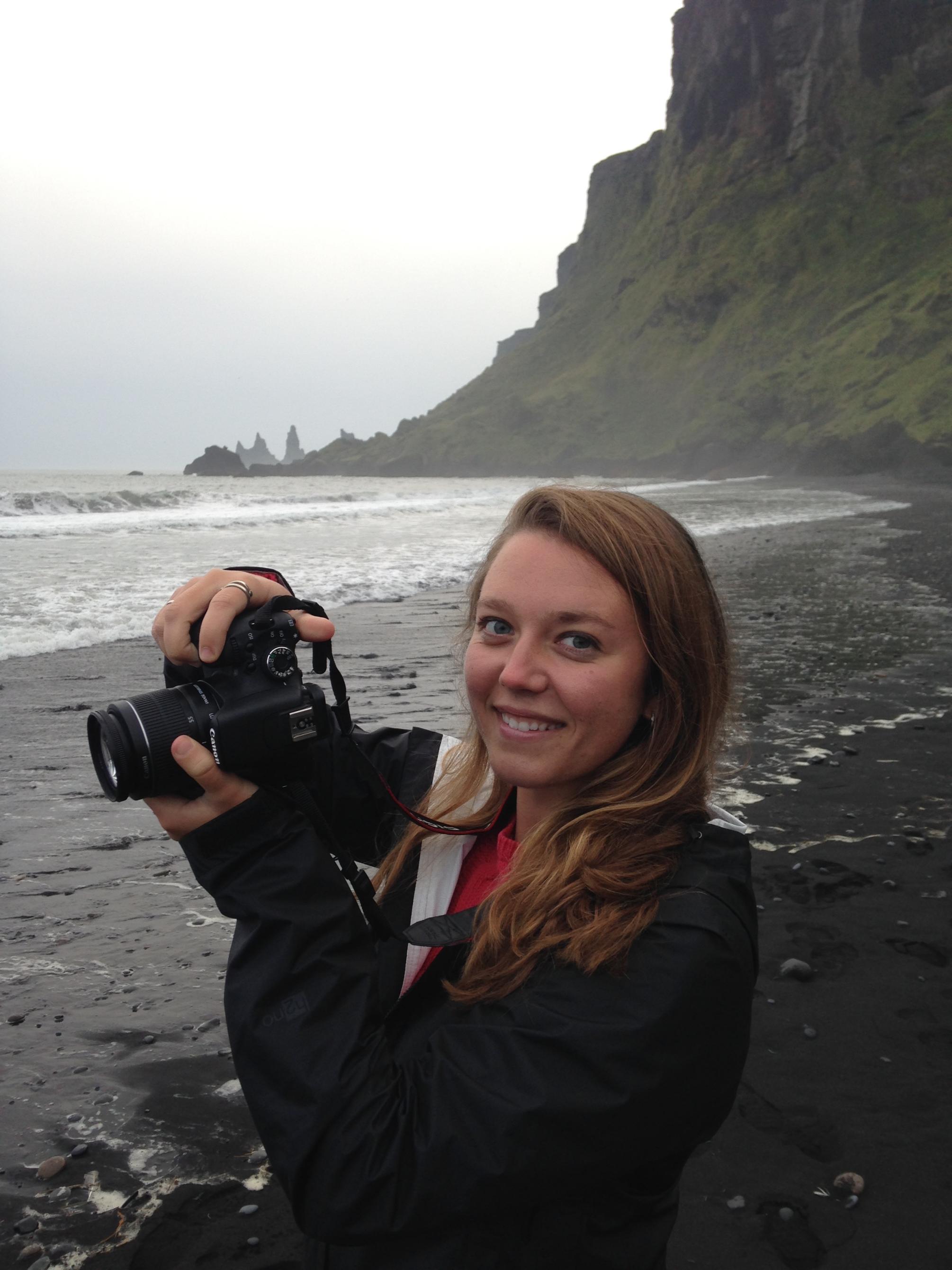 vertical photo of woman Sarah Eissler on cliffside beach holding camera