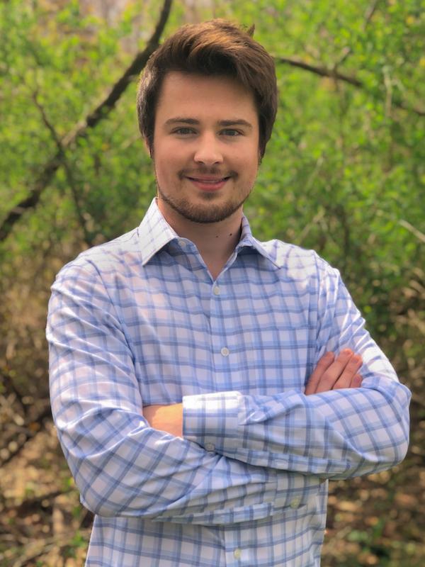 male student with arms crossed in business attire, poses for professional photo outside