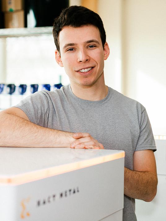 Portrait of Matt Woods leaning on Xact Metal 3D printer
