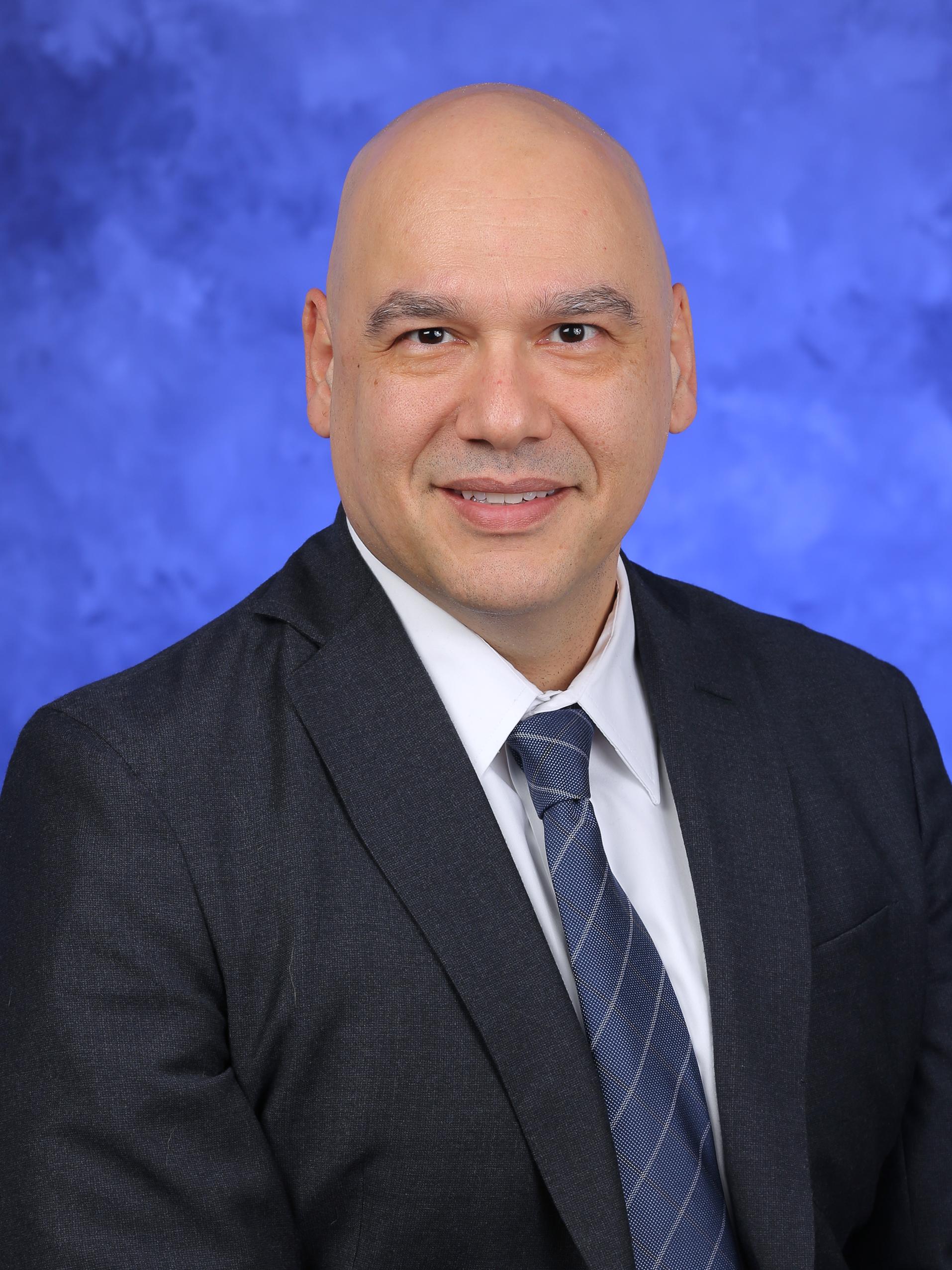 Dr. Safa Farzin poses for a professional headshot, wearing a suit and tie.