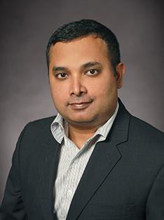 A man in a button-down shirt and dark suit jacket poses for a headshot.