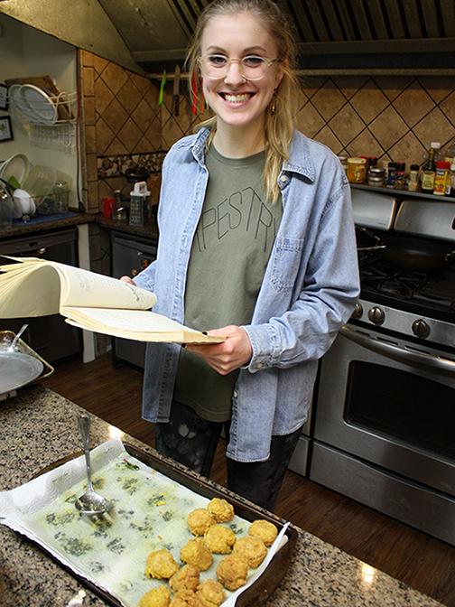Student in kitchen holding cookbook. 