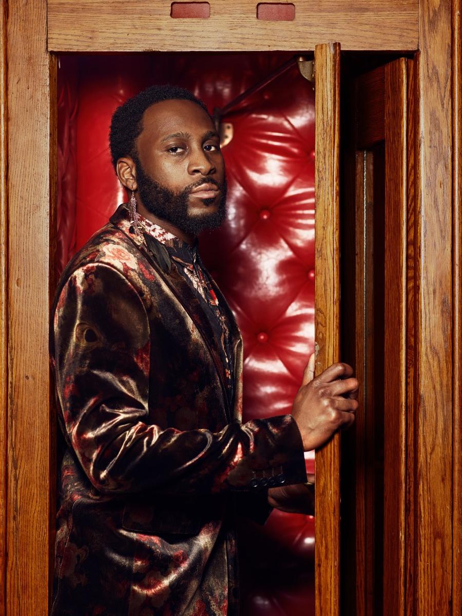 A man wearing a suit stands inside a wooden booth.
