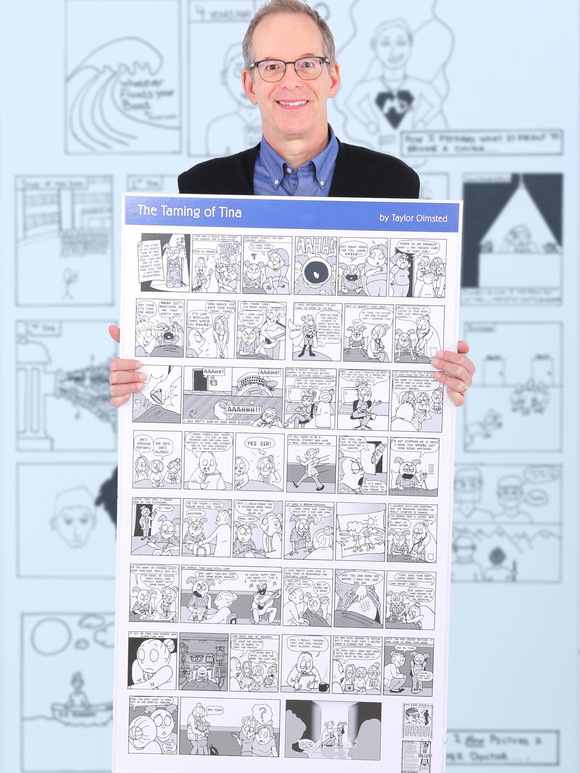 Dr. Michael Green, professor of humanities and medicine at Penn State College of Medicine, holds a posterboard with a comic titled “The Taming of Tina” by Taylor Olmstead. On the wall behind him are large cartoon comics.