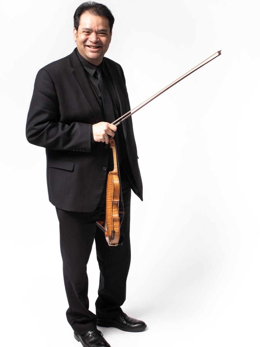 A man stands smiles while he holds his violin and bow.