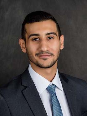 student in suit and blue tie smiles and poses for professional headshot photo