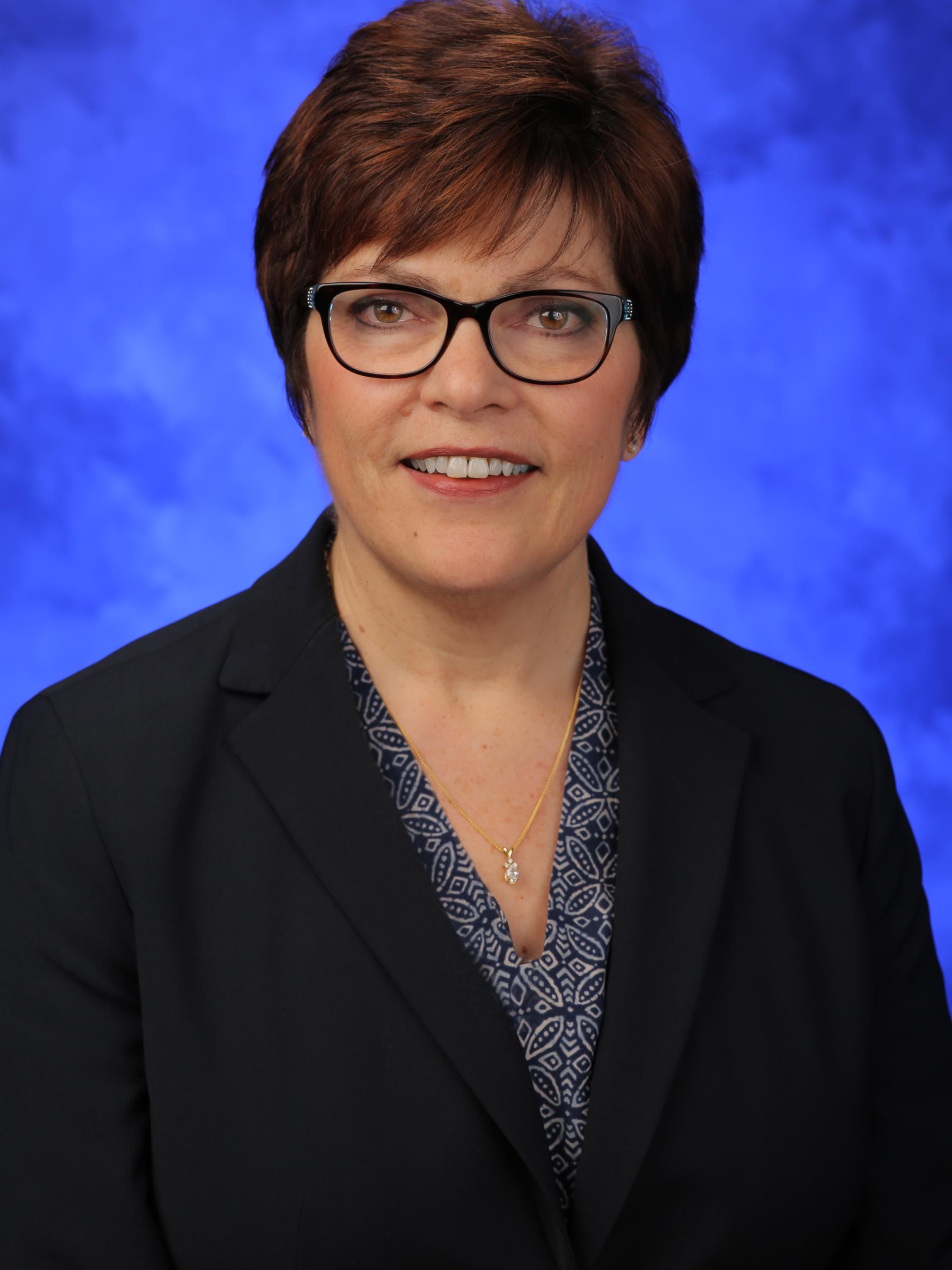 A headshot of Judy Himes, in front of a blue background.