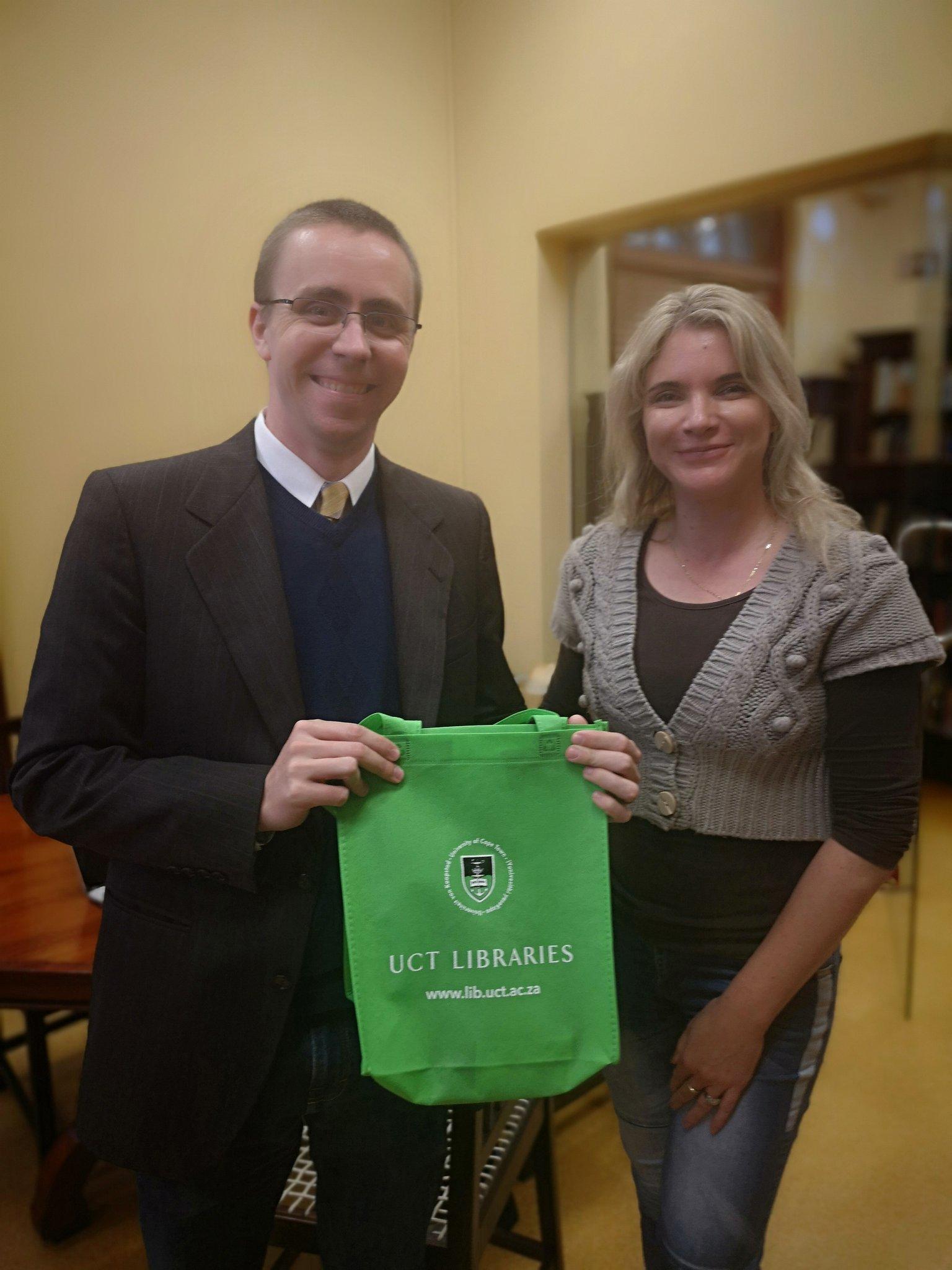 A man and a woman smiling and holding a University of Cape Town tote bag.