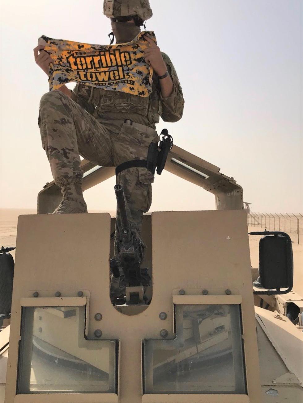 Man sits on M-ATV tank in desert holding Pittsburgh Terrible Towel