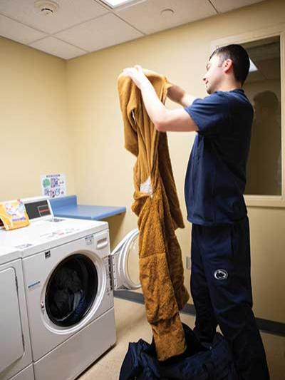 Zach Sowa holds up the Nittany Lion suit in front of a washing machine