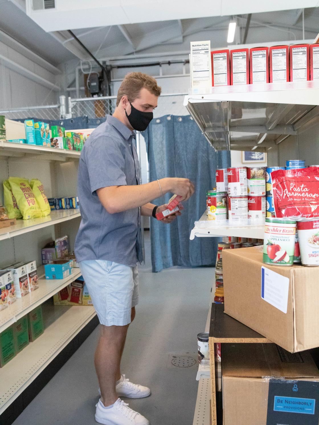 A college-aged male puts a grocery item on the shelf of the Penn State campus food bank, Lion's Pantry.
