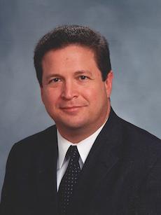 Man wearing a suit jacket and tie smiles. 
