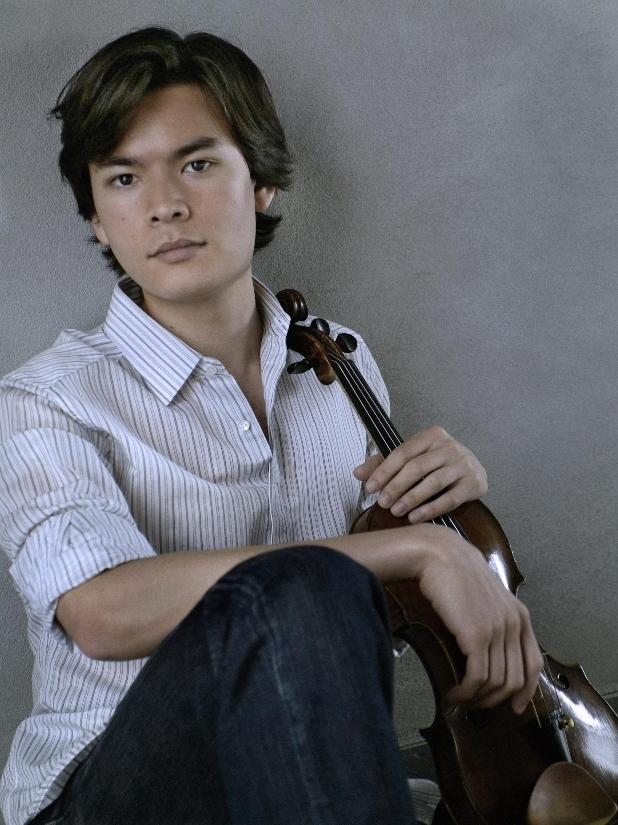 Stefan Jackiw leans against a wall and holds his violin.