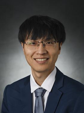 A man wearing glasses and a suit and tie smiles for a professional headshot.