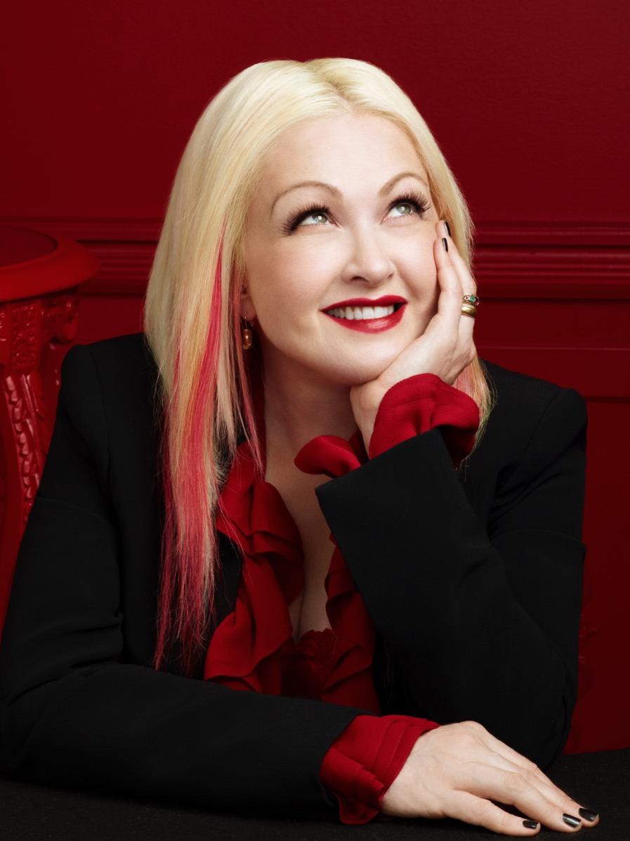A woman rests her chin in her hands while she looks upward and smiles.