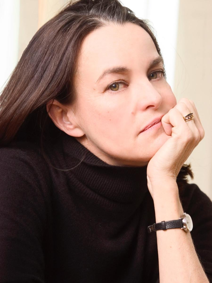 A woman rests her chin in her left hand while she looks sideways at the camera.