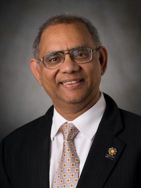 A head and shoulders photo of a man wearing a suit and tie and glasses. 