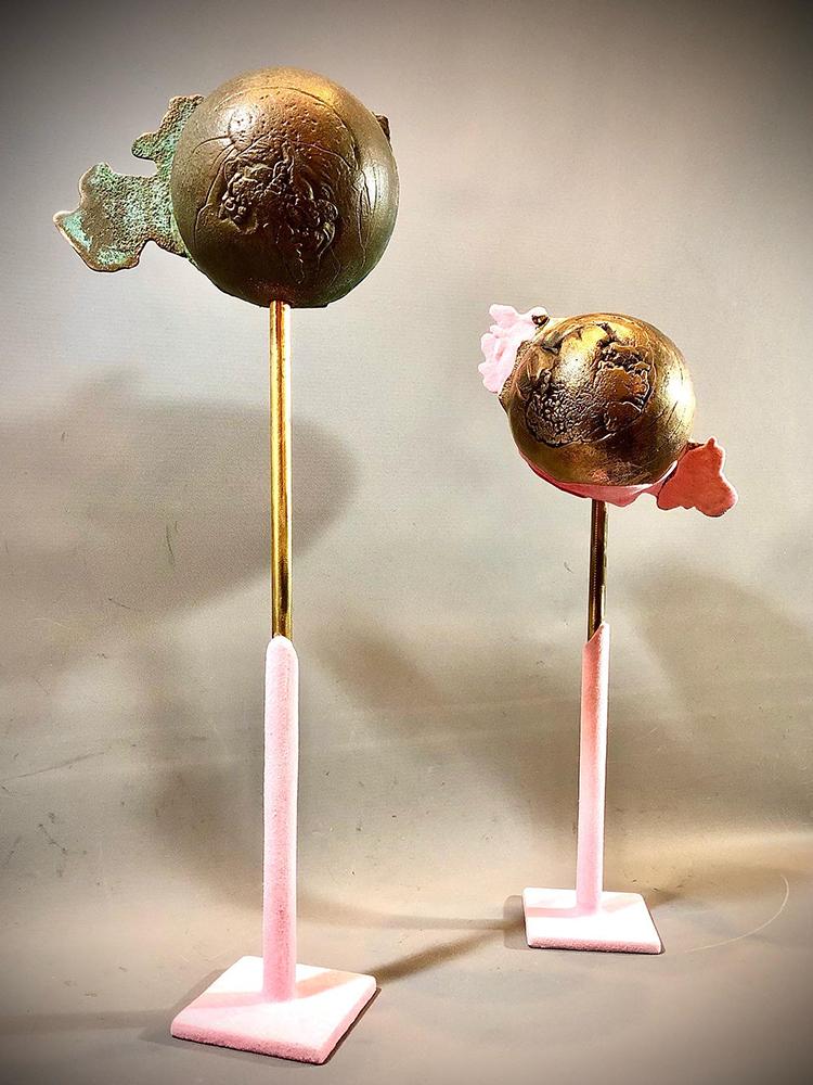 Two bronze globe-like sculptures on stands covered in part with pink felt