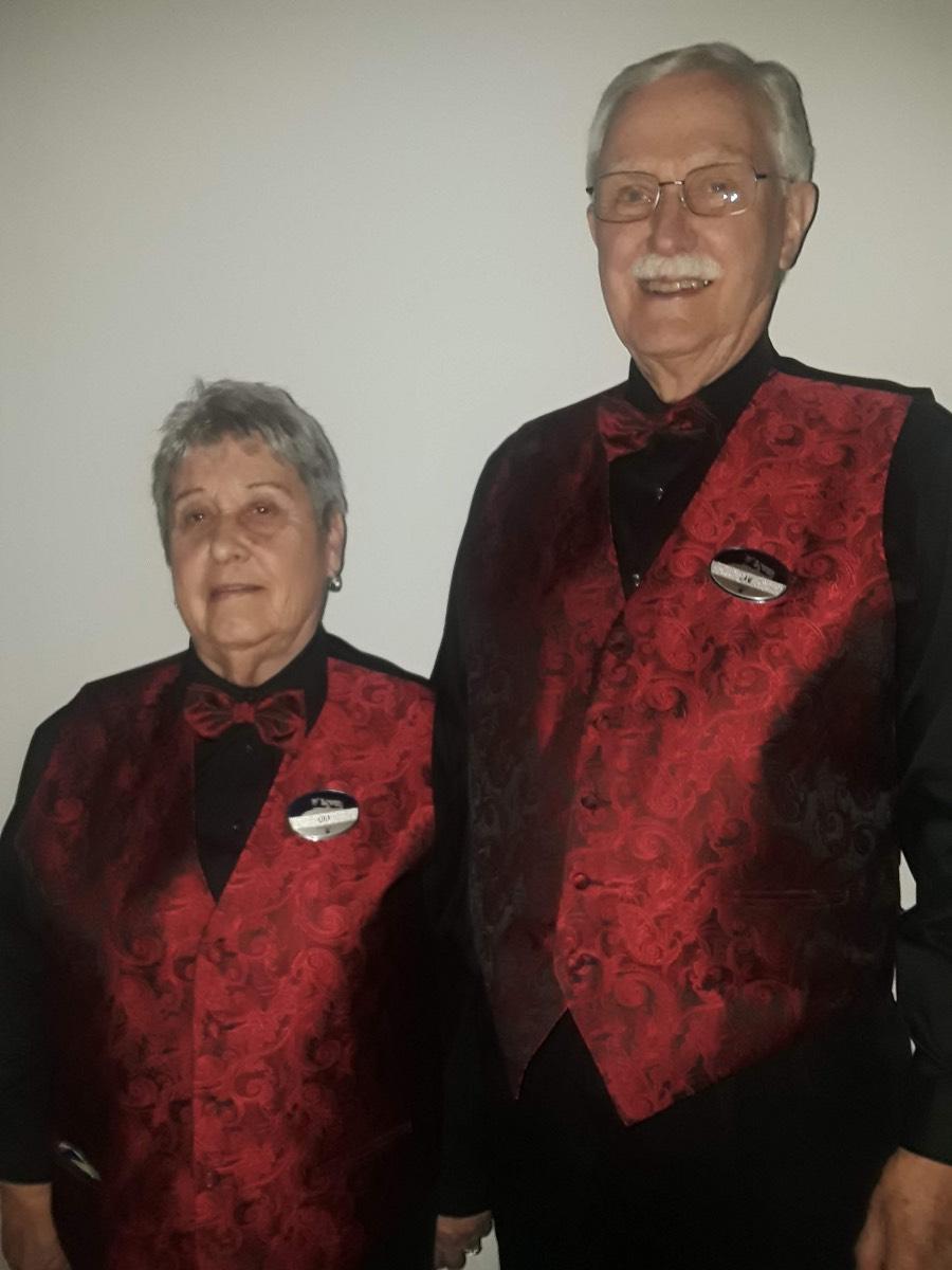 A woman and man waring identical usher uniforms smile for the camera.