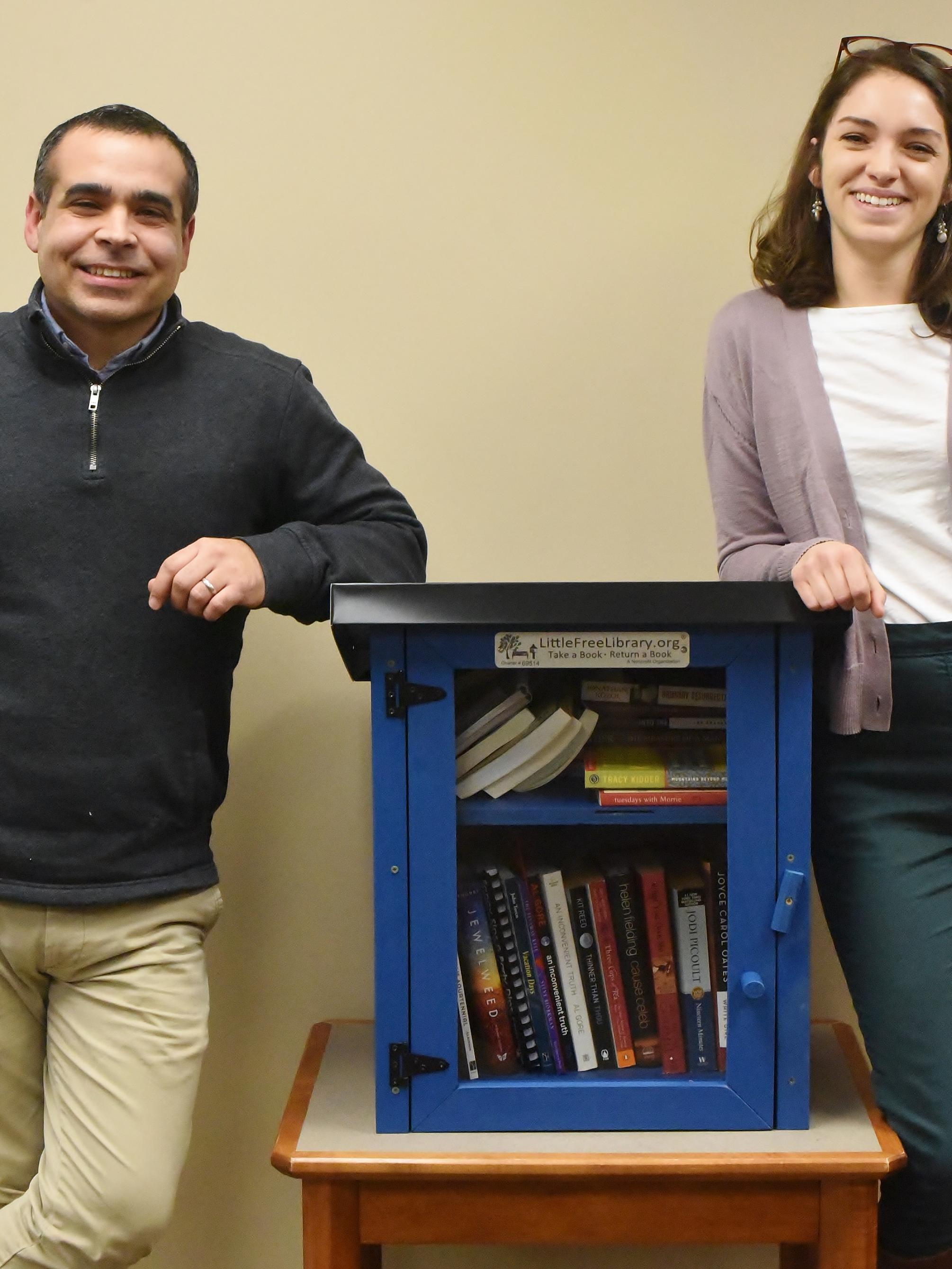 Two Penn State Behrend staff members stand next to one of the college's "Free Little Libraries"