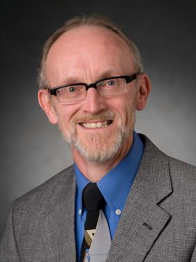 person wearing a suit and glasses smiles and poses for a professional headshot photo