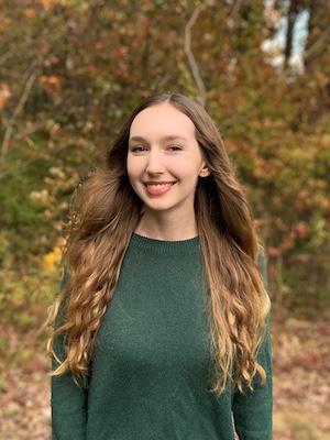 An engineering student smiles surrounded by fall foliage.