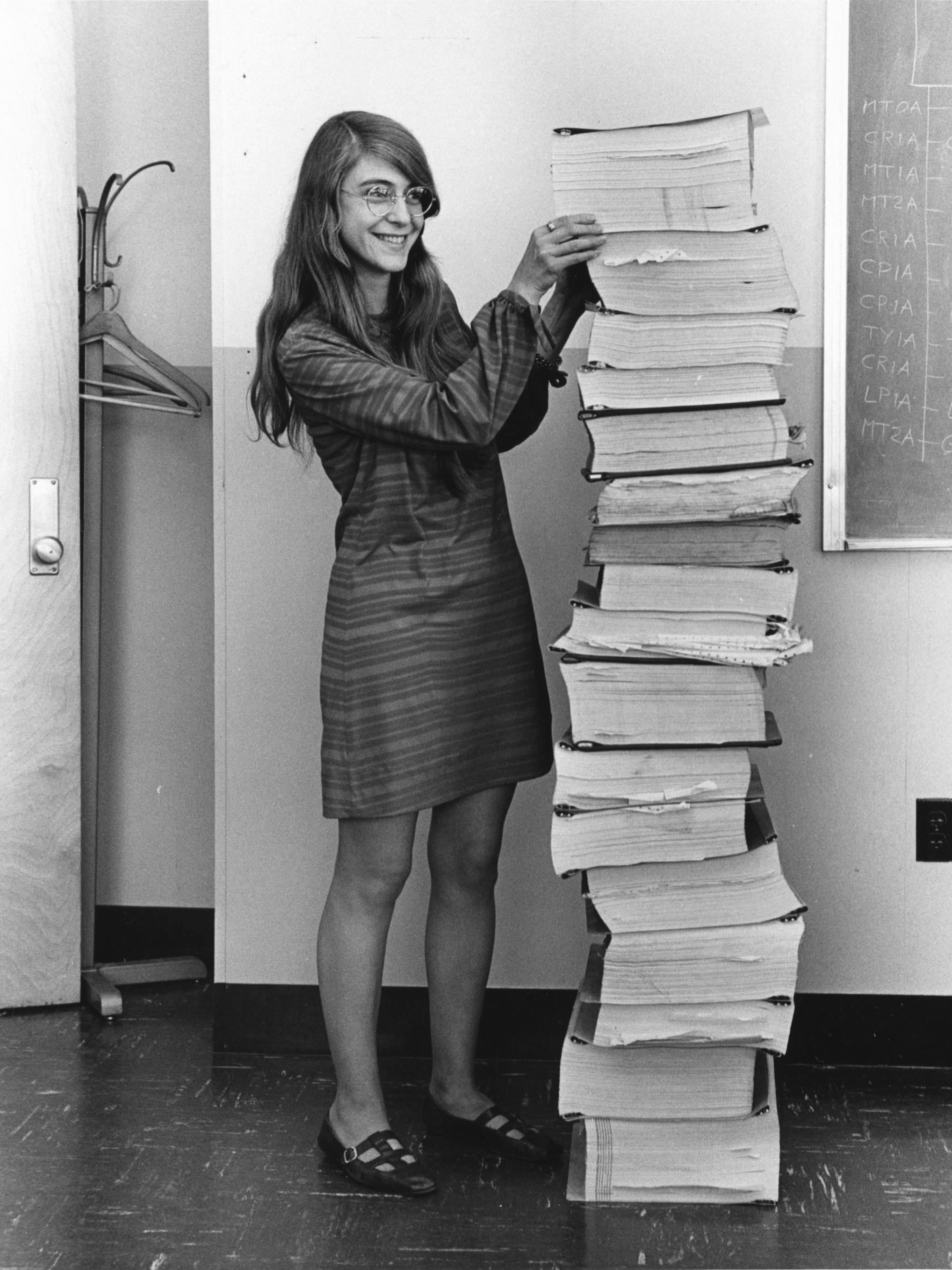 A woman stands next to a stack of books