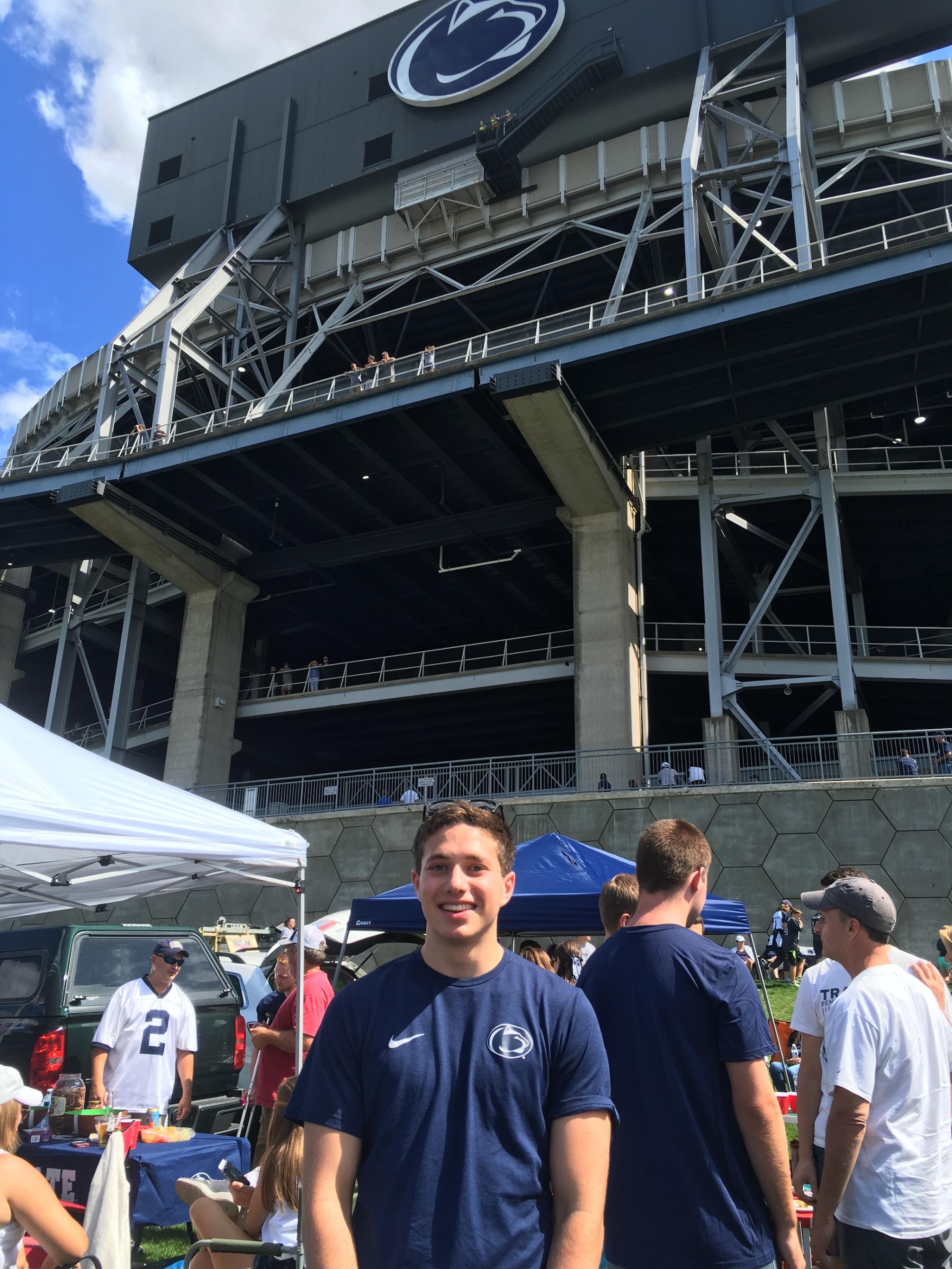 Young man stands before Beaver Stadium in blue on a football Saturday
