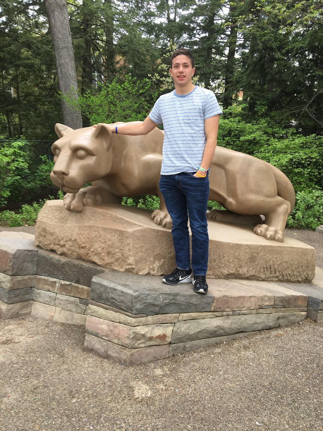 Young man sits in front of the Nittany Lion Shrine in grey