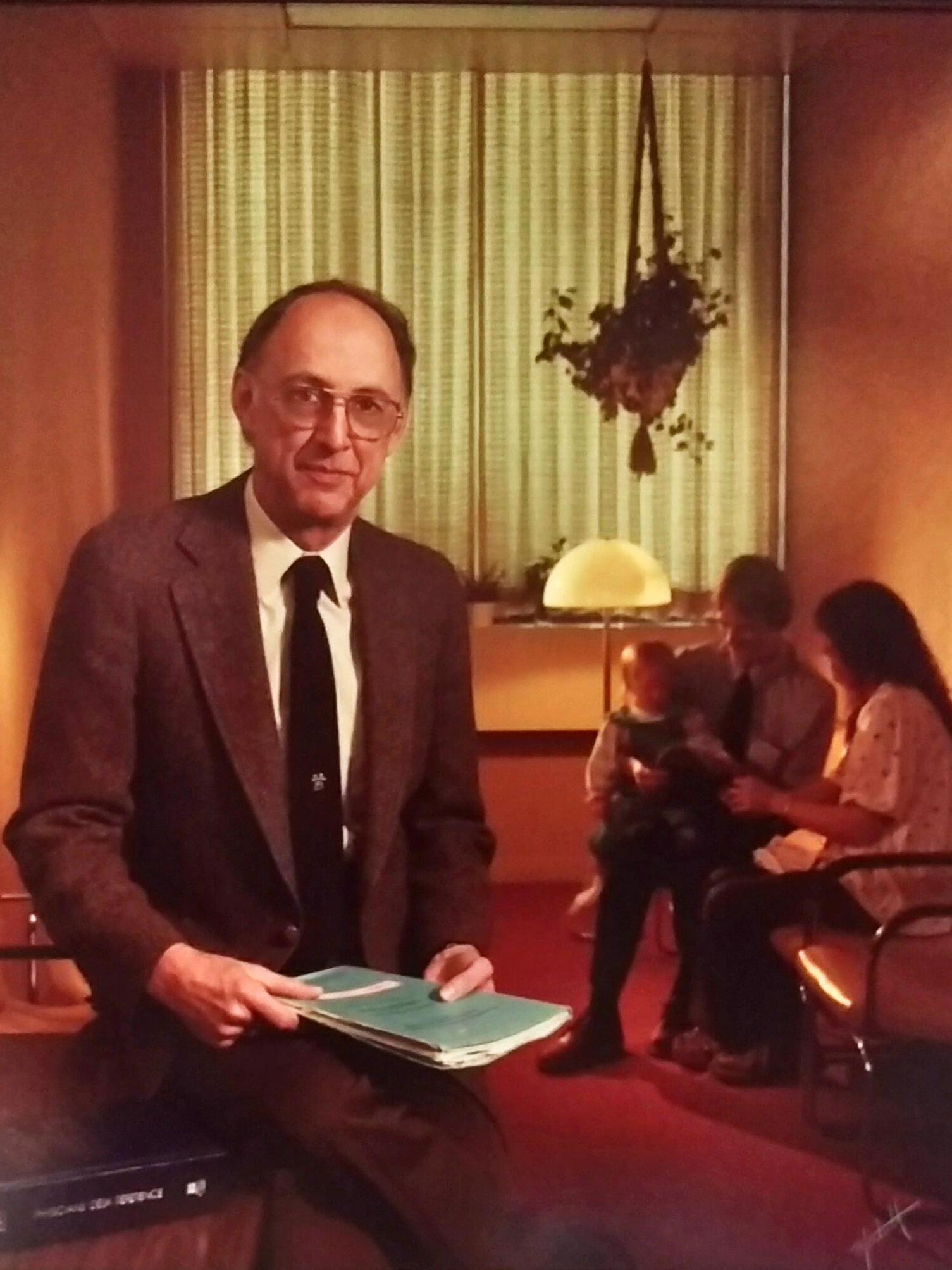 Dr. Thomas L. Leaman sits in the foreground; a couple with a young child is seen in the background.