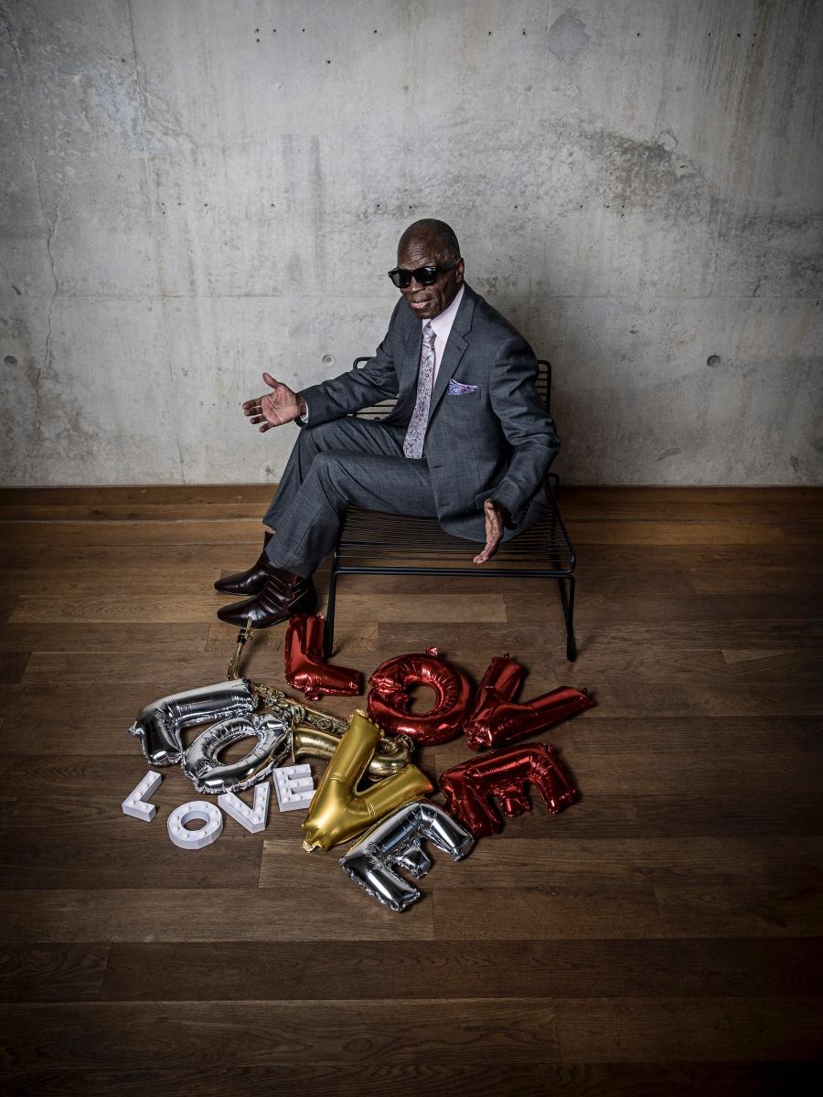 A man sits on a bench and is surrounded by inflated balloons spelling out the word "Love."