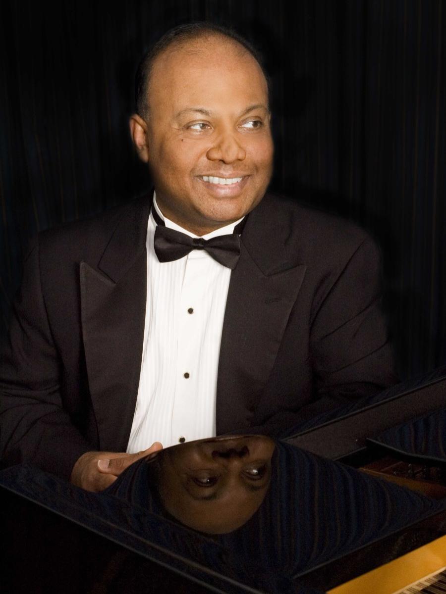 A man sitting in front of a piano smiles and looks to his left.