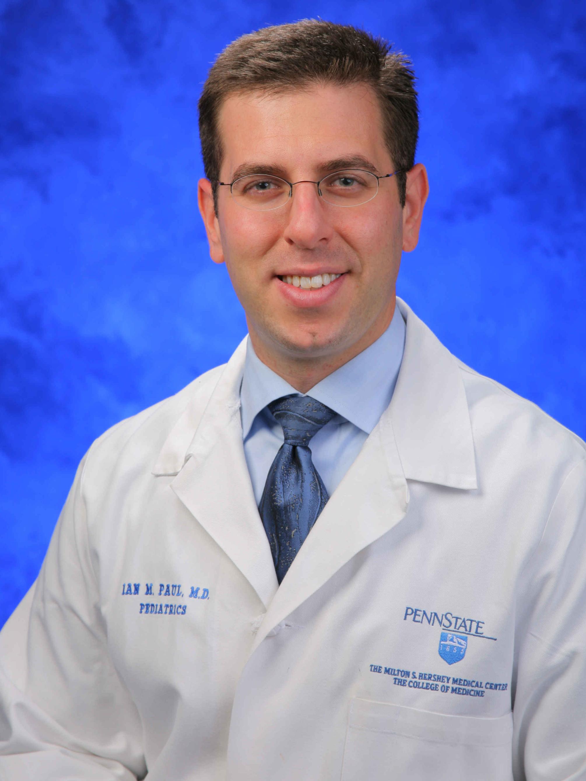 Dr. Ian Paul poses for a professional headshot photo, wearing a tie and physician's coat.