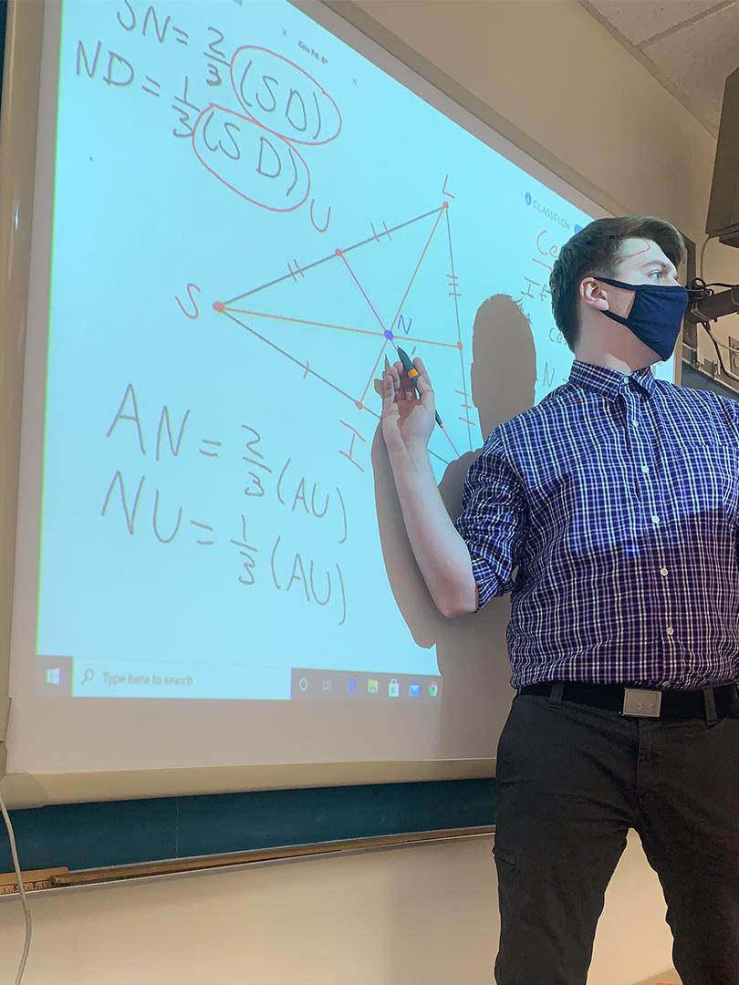 Student Teacher pointing at math problem on a projector while talking to class. 