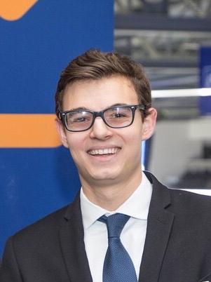 A young man with glasses smiles for a professional headshot. 
