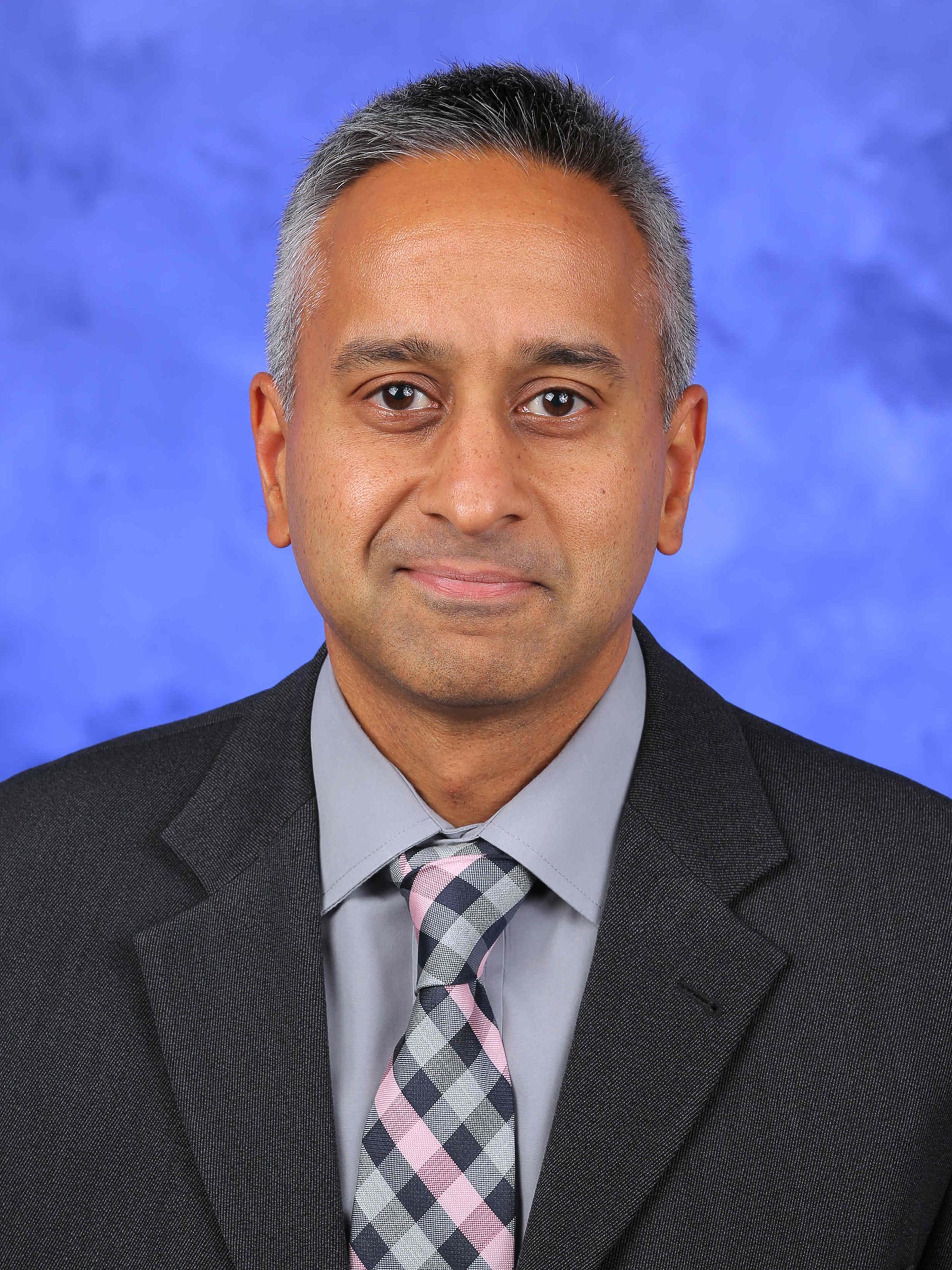 Dr. Jay Raman poses for a professional headshot wearing a suit and tie.