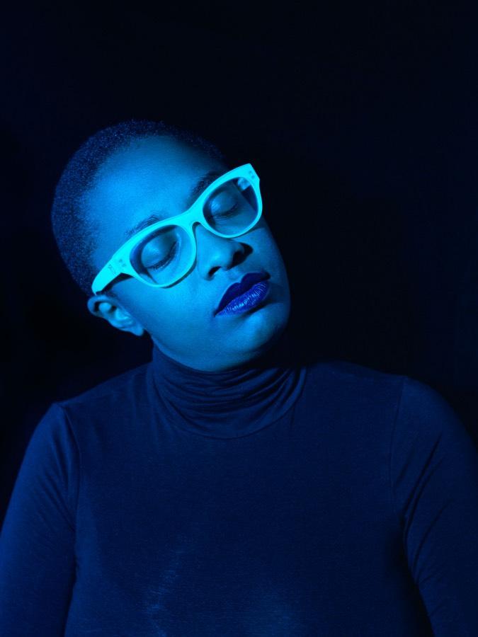 The singer, wearing thick-rimmed glasses, cocks her head to her right.